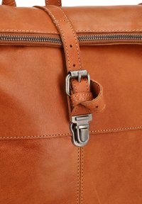 Borsa in pelle marrone chiaro con cuciture visibili, zip in metallo e chiusura in argento fissata da una tracolla in pelle con fori per fibbie.