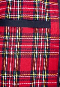 Primer plano de una tela de cuadros roja con líneas amarillas, blancas y negras que presenta una abertura horizontal para bolsillo de color negro.