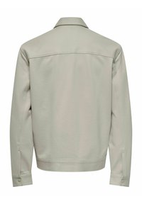 Veste beige clair à manches longues avec un col, des poignets à bouton et une couture horizontale dans le haut du dos.