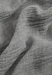Tissu gris doux avec un tissage fin et texturé, délicatement plié et drapé, montrant des ombres subtiles et des reflets sur la surface du matériau.