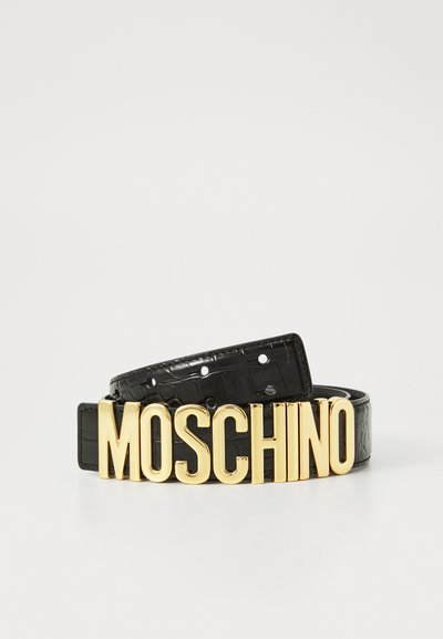 Cinturón de piel negra con textura de cocodrilo y un gran logo dorado de "MOSCHINO" como hebilla. Presenta múltiples agujeros de ajuste.