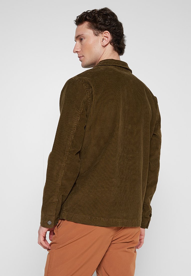 Brązowa kurtka z korduroju z kołnierzykiem, długimi rękawami i zapięciem na guziki przy mankietach. Teksturowany materiał z pionowymi prążkami i luźnym krojem.