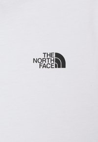 Bílý bavlněný tričko s černým logem na levé části hrudi, zobrazující "THE NORTH FACE" a polo-kruhový designový prvek.