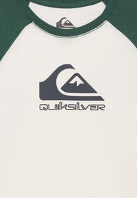 Short-sleeve t-shirt with a white body and green raglan sleeves. Features a black "Quiksilver" logo and mountain graphic. Cotton material.