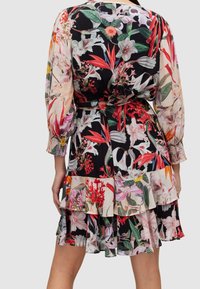 Robe fleurie avec un fond noir, ornée de fleurs rouges et roses vives, à manches bouffantes longues et détails de volants superposés au bas.