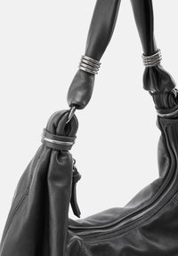 Zwarte lederen handtas met een nonchalant ontwerp, voorzien van een brede schouderband en metalen accenten. Ritsdetail zichtbaar.