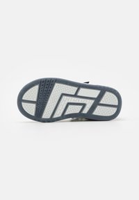 Suela de una zapatilla que presenta un material de goma texturizado en azul oscuro y blanco, con un patrón de zigzag prominente y agarres de tracción.