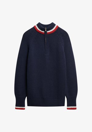 Granatowy sweter z dzianiny z wysokim kołnierzem, z zamkiem błyskawicznym na ćwierć długości z przodu oraz kontrastującymi czerwonymi i białymi paskami na kołnierzu i mankietach.