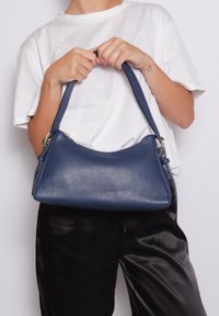 Marineblauwe leren schoudertas met een gestructureerd oppervlak, een halvemaanvorm en één schouderband; beschikt over een ritssluiting en metalen hardware-accenten.