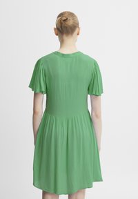 Robe courte à manches courtes de couleur vert clair avec une texture lisse, un corsage ajusté et une jupe évasée. Encolure simple et détails froncés aux manches.