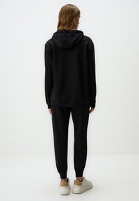 Czarna bluza z kapturem i dopasowane zwężane spodnie dresowe, wykonane z miękkiego materiału. Białe sneakersy z beżowymi akcentami dopełniają strój.