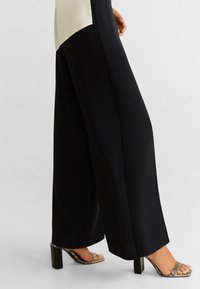 Sorte bukser med bred benvidde kombineret med højhælede sandaler med metalaccent, der har en glat tekstur og en elegant silhuet.