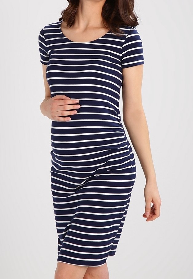 Femme enceinte portant une robe à manches courtes rayée bleu marine et blanc, tenant doucement son ventre d’une main.