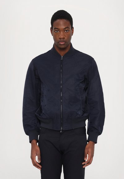 Chaqueta bomber de la marina con cierre de cremallera en el frente, puños y cinturilla acanalados. La tela suave y ligera presenta un sutil patrón en relieve.