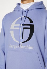 Felpa con cappuccio viola realizzata in tessuto misto cotone, caratterizzata da un logo grafico prominente in nero e grigio, con dettagli in cordoncino argentato.