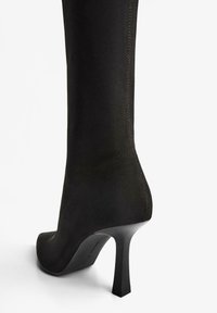 Czarne, zamszowe botki na wysokim obcasie, charakteryzujące się eleganckim designem, spiczastym noskiem oraz kwadratowym obcasem z widocznym przeszyciem po bokach.