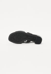 Sandale à talons ouverte noire avec une semelle en caoutchouc texturée, dotée de deux larges brides et d'un talon bloc. Fini lisse avec un minimalisme dans les détails.