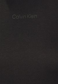 Czarna bawełniana tkanina o prążkowanej fakturze, z delikatnym nadrukiem marki "Calvin Klein" w jasnoszarym kolorze rozproszonym po powierzchni.