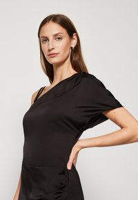 Melnas satīna kleita ar vienu plecu, elegants dizains, īsām piedurknēm un pieguļoša silueta. Gluda tekstūra, minimālistiska apdare un vienkārša griezuma.