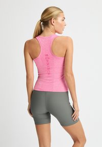 Verenka vaaleanpunainen urheiluhihaton paita, jossa on teksturoitu kuvio ja urheilullinen racerback-muotoilu, sekä logotulos selässä, yhdistettynä harmaisiin shortseihin.