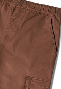 Pantaloni cargo marroni con una cintura elastica, dotati di una tasca laterale e dettagli cuciti. Texture liscia con una leggera lucentezza.
