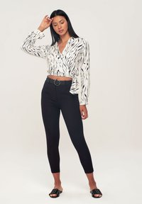 Blusa avvolgente bianca e nera con maniche lunghe e dettaglio con fiocco in vita, abbinata a pantaloni neri aderenti e sandali neri con fasce.
