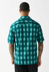 Cămașă cu mâneci scurte în nuanță de teal, având un model în carouri cu nuanțe variate, croi lejer și guler.