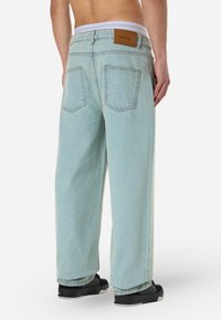 Svetlomodré džíny so širokými nohavicami a vysokým pásom, s dvoma zadnými vreckami a hnedou koženou nášivkou na páse. Textúrovaný denimový materiál.
