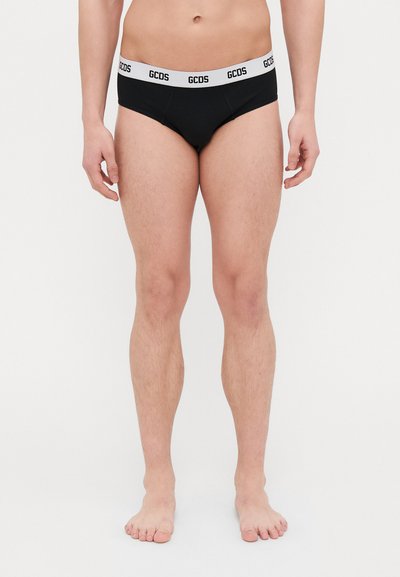Black men's briefs with a white elastic waistband featuring "GCDS" logo. The fabric is smooth with a snug fit, and the design is minimalist.
