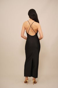 Black dress with a fitted silhouette, open back, thin crisscross straps, white polka dots, and a thigh-high side slit. Smooth texture.
