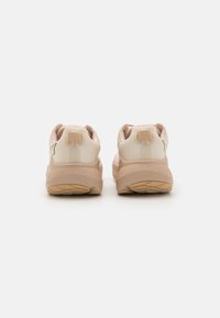 Beige athletic shoes with a textured upper, rubber sole, and padded collar. Features a soft mesh design and minimal branding on the back.