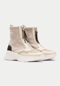 Botas de tobillo de ante y cuero beige con suela gruesa blanca, que cuentan con cremalleras laterales y borlas marrones. Detalles texturizados en los laterales.