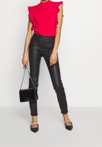 Červená halenka s volány, černé úzké kalhoty z umělé kůže, černá kabelka s řetízkovým páskem a černé lodičky s špičatou špičkou zdobené kamínky.