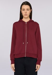 Sudadera con cremallera en color burdeos, hecha de un suave tejido texturizado. Presenta una capucha con cordón, puños acanalados y un logo discreto en el pecho.