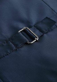 Dunkelblaues Stoffmuster im Nahbereich mit einer silbernen Metallspange. Das Material hat eine glatte Textur mit dezenten Nähten und einem rechteckigen Riemen.