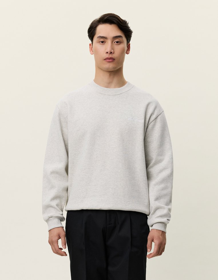 Šviesiai pilkas paprastas megztinis su gaubtu ir rankovėmis, turintis mažą logotipo detalę krūtinėje, pagamintas iš minkštos medvilnės mišinys.