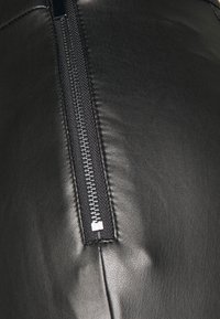 Tissu en cuir noir avec une fermeture éclair noire bien visible sur un côté, dotée d'une languette en métal et d'une texture subtile à la surface.