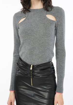 Femme portant un pull gris à manches longues avec des découpes aux épaules et une jupe en cuir noire froncée taille haute avec une fermeture éclair dorée à l'avant.