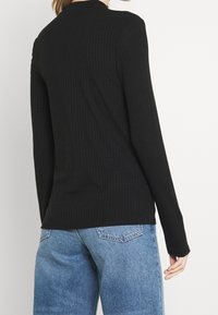 Svart ribbad långärmad topp med rundad halsringning, i slim fit och textilerat tyg, tillsammans med ljusblå denimjeans.