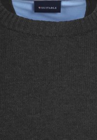 Schwarzer Strickpullover mit geripptem Ausschnitt und strukturierter Oberfläche. Etikett am Kragen innen sichtbar. Material wirkt weich und flexibel.