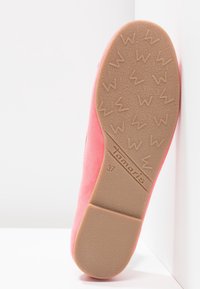 Zapato de ante rosa con suela plana. La suela presenta un patrón de agarre texturizado y el nombre de la marca "Tamaris" grabado junto con la talla "37."