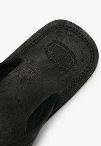 Sandale en cuir noir avec bords cousus et nom de marque embossé "SUPERDRY" sur la semelle intérieure, affichée sur fond blanc.