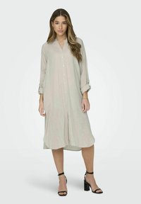 Ljus beige lång skjortklänning i linne, med krage, framknäppning, uppkavlade långa ärmar och en avslappnad passform. Bärs med svarta klacksandaler.