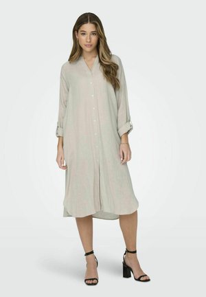 Ljus beige lång skjortklänning i linne, med krage, framknäppning, uppkavlade långa ärmar och en avslappnad passform. Bärs med svarta klacksandaler.