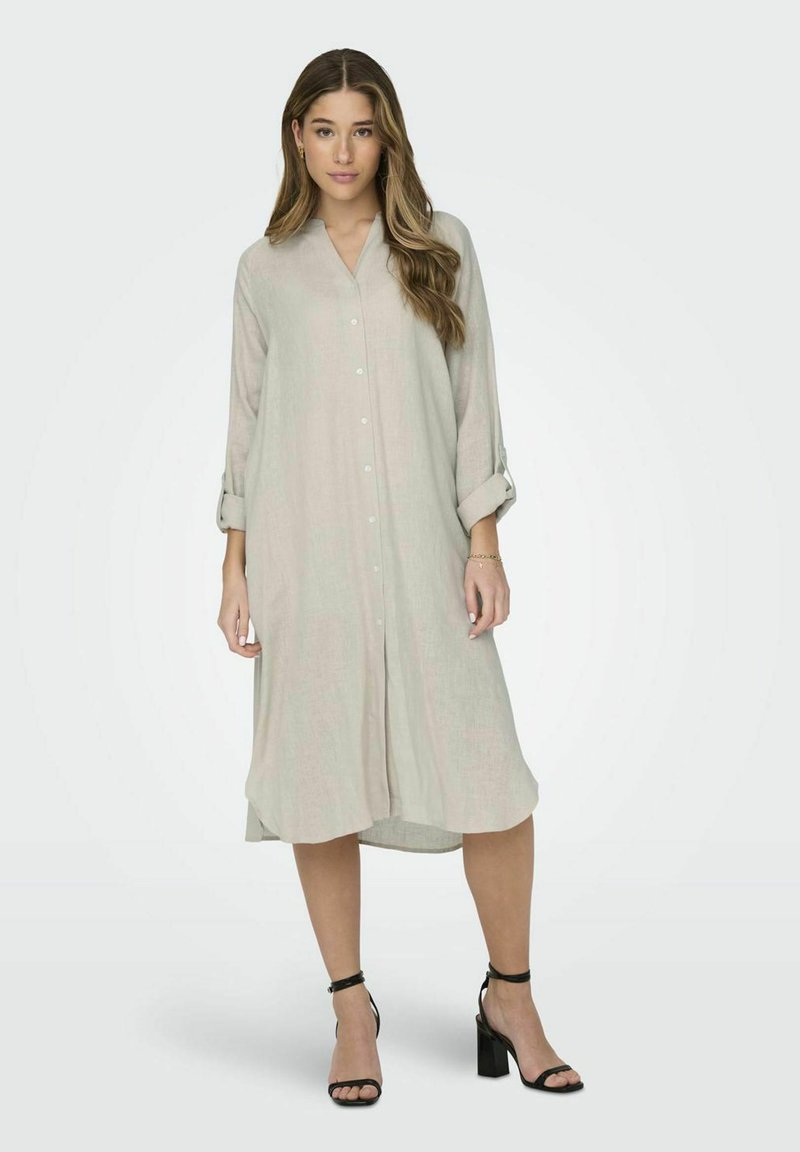 Ljus beige lång skjortklänning i linne, med krage, framknäppning, uppkavlade långa ärmar och en avslappnad passform. Bärs med svarta klacksandaler.