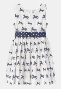 Vit ärmlös klänning med midjebälte i marinblått med prickar och marinblå hästmönster jämnt fördelade över tyget.