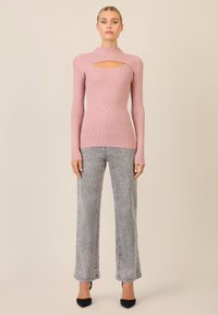 Langärmliges, rosa Ripp-Oberteil mit Ausschnitt, kombiniert mit hellgrauen, gepunkteten Schlagjeans und schwarzen hohen Schuhen. Glatte Textur, figurbetontes Design.