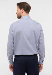 Langsleeve shirt met blauw en witte verticale strepen, voorzien van een strakke kraag en met knoopsluitingen bij de manchetten. Zachte textuur met een getailleerde pasvorm.