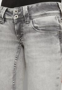 Úzké šedé džíny s vybledlým texturem, s dvojitým zapínáním, předními kapsami a viditelnými švy.