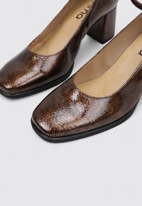 Zapatos de cuero marrón con tacón cuadrado, diseño de punta cuadrada y un acabado texturizado y brillante. El interior cuenta con un forro y suela beige.